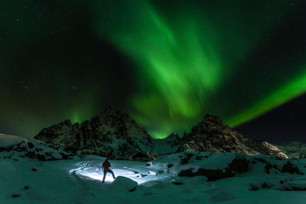 Wanderer im magischen Nordlicht auf den Lofoten, Norwegen. Foto: bonciutoma - stock.adobe.com